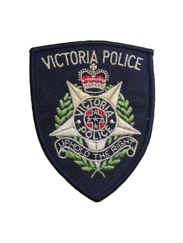 An embroidered Victoria Police badge patch on a wooden surface next to a ruler for scale.